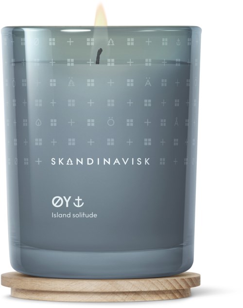 Een grijze kaars in glas op een houten onderzetter, gemarkeerd 'Island solitude' door Skandinavisk, met een zwarte lont.