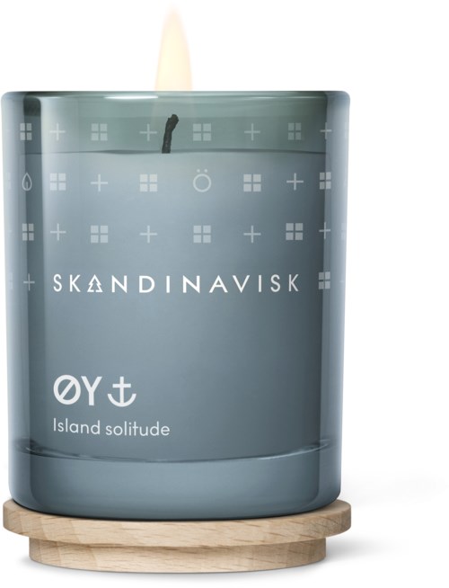 Gray candle in glass with Scandinavian logo and text, on a wooden base, candle wick is lit.