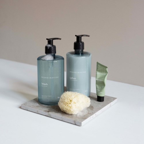 Two blue skincare bottles, a small green tube, a sponge, on a marble tray.