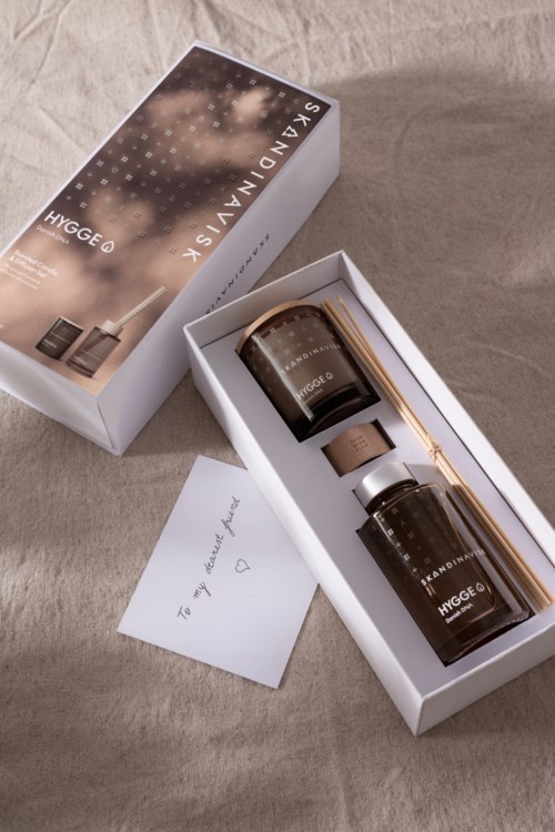 Ein Geschenkset mit Kerzen, einem Zettel und einer Box, auf einem beigen Tuch.