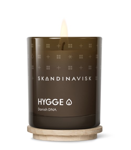 A dark brown candle with a wooden base, labeled "SKANDINAVISK" and "HYGGE Danish DNA," with a flame on top.