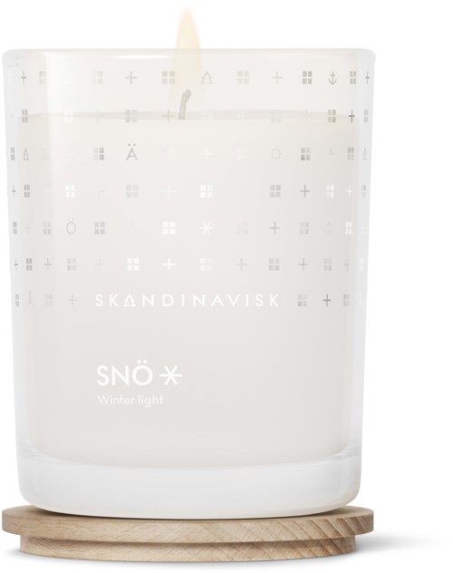 Een witte kaars in een glazen houder, met label 'Skandinavisk' en 'Snö Winter Light', op een houten onderkant.
