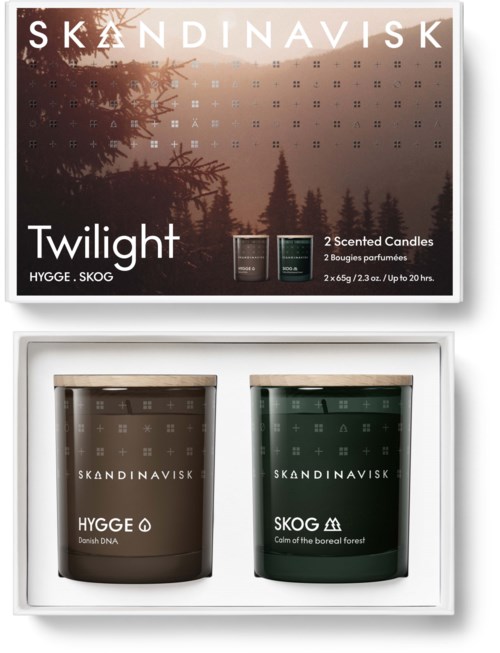 Förpackning med två doftljus, ett brunt märkt 'HYGGE' och ett grönt märkt 'SKOG', för en mysig skogskänsla eller hemmet.