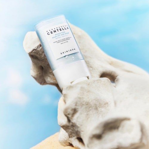 A skincare product bottle held by a white sculpture against a bright blue background.