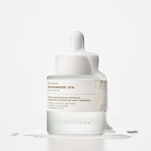 En klar glasflaske med hvid drophætte, indeholder et hudpleje seruml mærket Niacinamide 10%. lidt serum er spildt omkring.