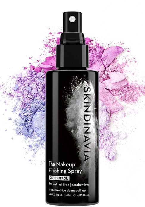 Czarna butelka z rozpylaczem z napisem 'The Makeup Finishing Spray' z fioletowymi i różowymi pyłkami za nią.
