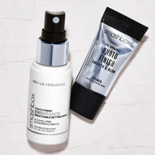 A spray bottle and a tube of primer from Smashbox, used for makeup. The spray is white with black and silver.