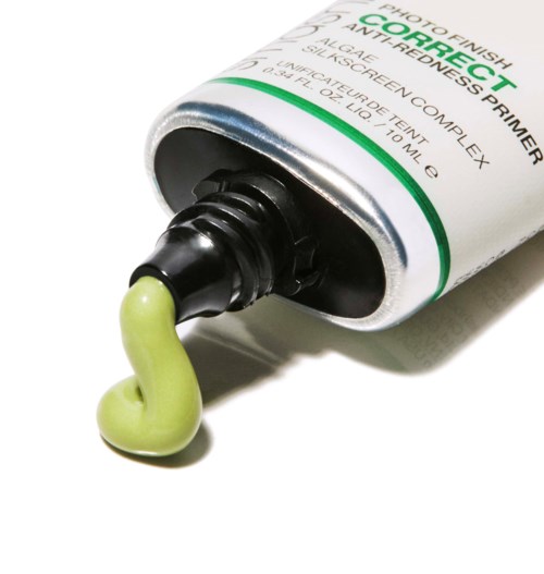 En tub med grönt färgkorrigerande primer med lite produkt som kommer ut och en vit bakgrund.
