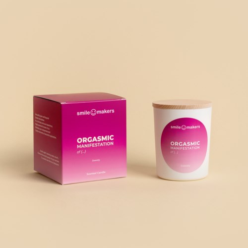 Ett ljus i en vit behållare med en rosa och vit etikett, bredvid en rosa låda, båda med texten "Orgasmic Manifestation."