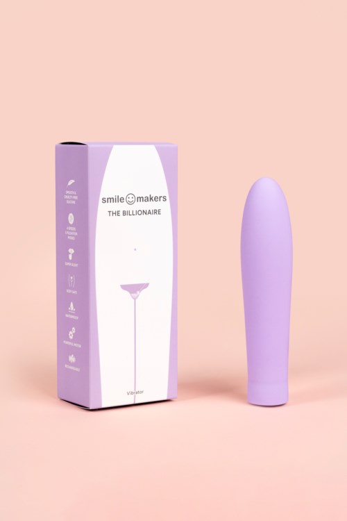 En lila vibrator står bredvid en lila och vit box med text på, mot en rosa bakgrund.
