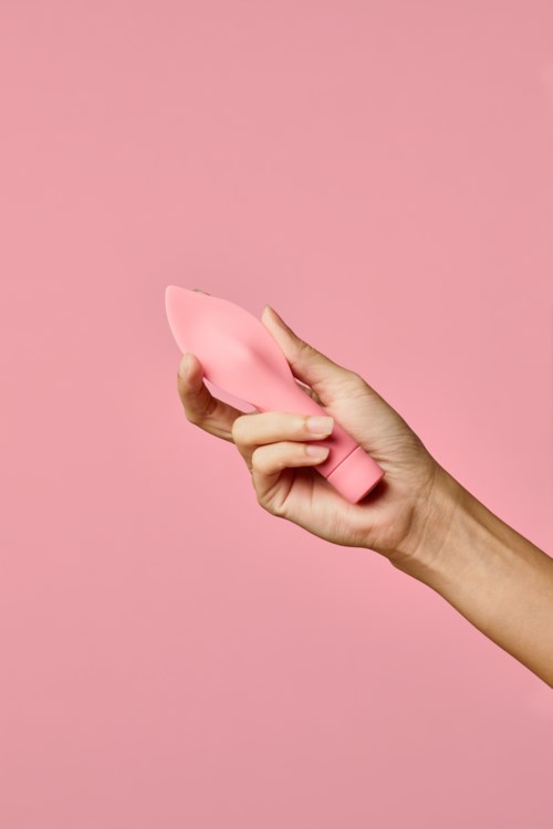 En hånd holder en rosa rengjøringsbørste mot en matchende rosa bakgrunn.