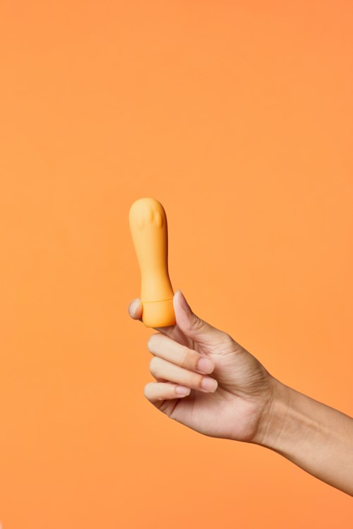 En hånd som holder et gult objekt formet som en finger mot en oransje bakgrunn.