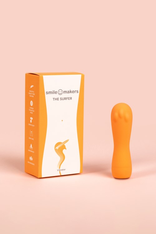 En lys orange, formet genstand ved siden af en æske med mærket "Smile Makers The Surfer" på en lyserød baggrund.