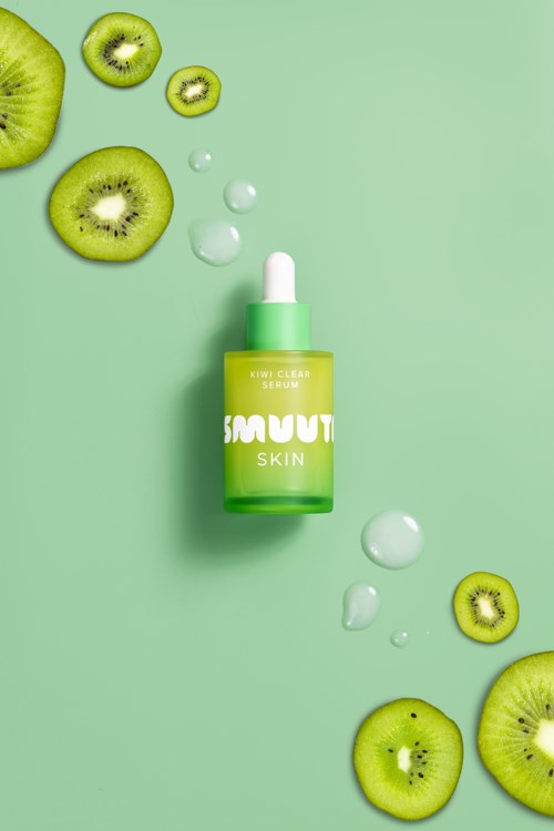 Zielona butelka serum na skórę otoczona pokrojonymi kiwi i kroplami na jasnym zielonym tle.