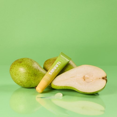 Two whole pears, one half-cut pear, and a green tube of skincare product on a green background.