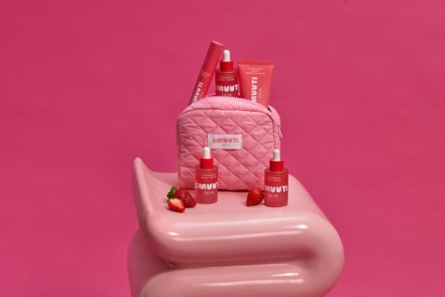 Rosa hudvårdsprodukter med jordgubbar på en rosa bänk mot en rosa bakgrund.