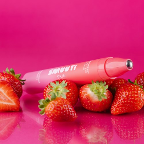Jordgubbar omringar en rosa ansiktsrullare för hudvård på en rosa bakgrund.