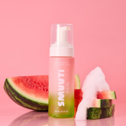 A pink and green bottle of skincare with watermelon slices and foam around it.