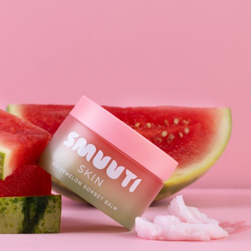 Ein Glas Wassermelonen-Sorbet-Balm lehnt an Wassermelonenstücke mit rosa Hintergrund.
