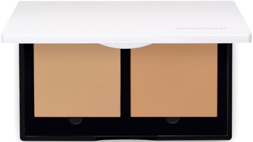 To beige makeup-pudder med svarte kanter i et hvittu rom. Kassen har et skyvedeksel.