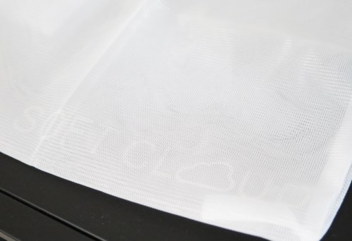 Ett vitt papper eller tyg med ett subtilt texturerat mönster, delvis över en mörk yta.