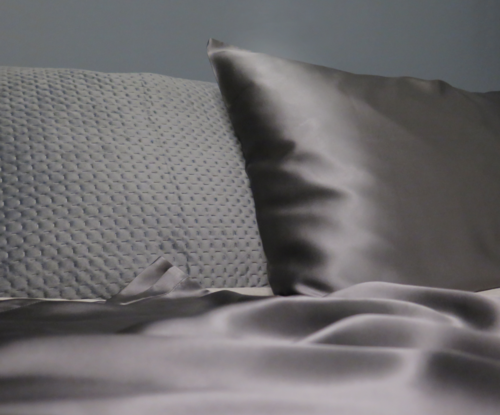 Two pillows, one textured and one smooth, on a bed with a silky blanket.