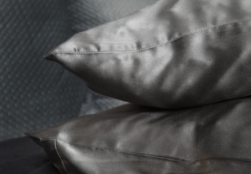 To mørkegrå satin puffer stablet mod en tekstureret mørk baggrund.