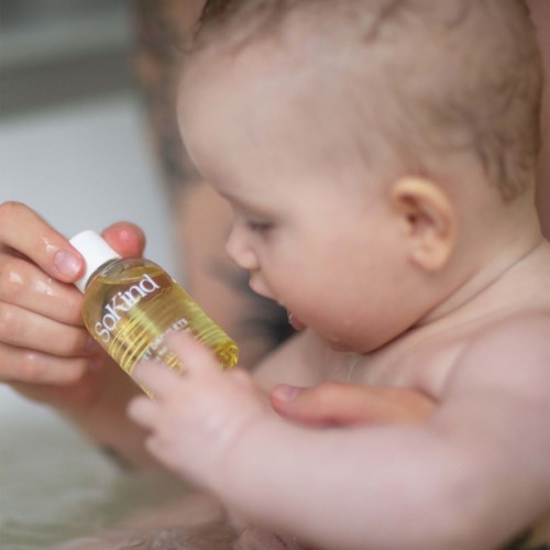 En bebis får medicin eller olja i en liten flaska av en vuxen. Bebisen är i ett bad eller liknande.