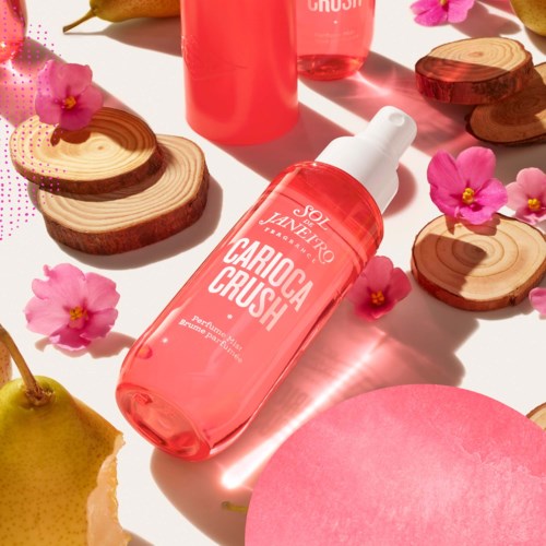 Pink skincare bottle surrounded by wood slices, pink flowers, and a partly sliced lemon.