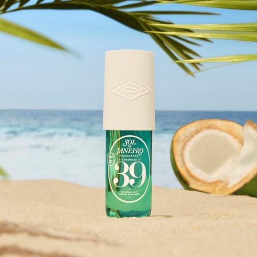 En flaske med solkrem på stranden med kokosnøtt og hav i bakgrunnen.