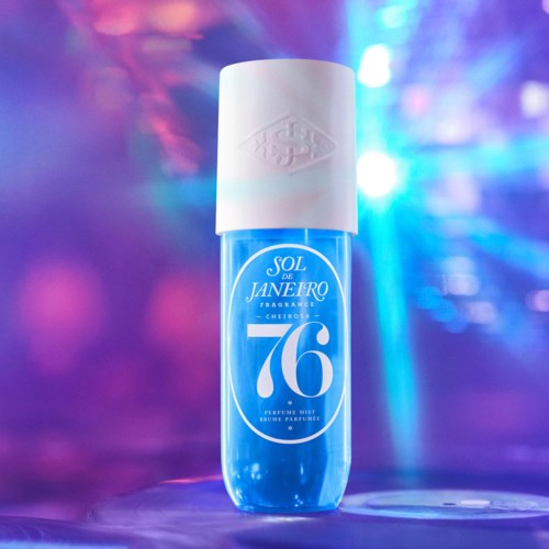 Een blauw parfumfles met witte dop en etiket, staat op een oppervlak met kleurrijke lichten op de achtergrond.