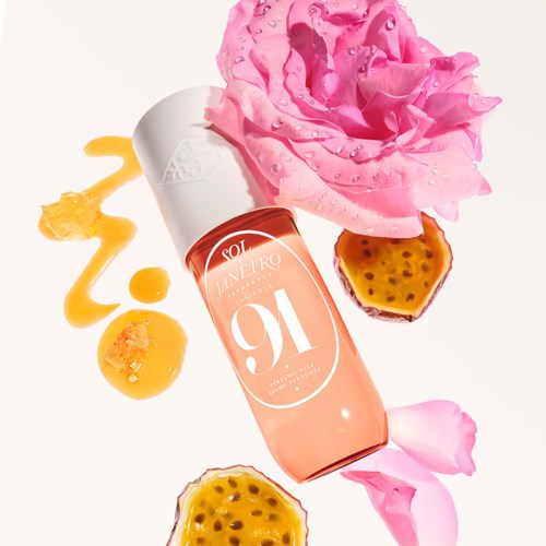 A pink flower, passion fruit halves, and a bottle of skincare serum with some drops and drips around it.