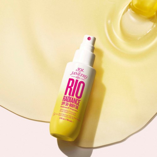 A yellow and white bottle of Rio Radiance body oil with SPF stands on a light yellow surface.