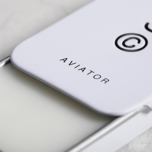 En hvid enhed med ordet 'AVIATOR' og et copyright-symbol, forbundet med et kabel.