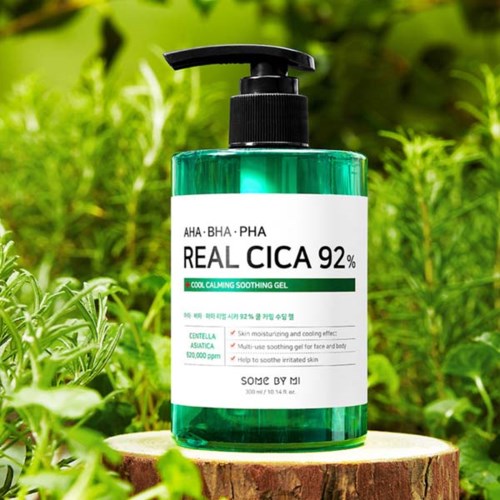 A green bottle of soothing gel labeled 'Real Cica 92%' stands on a tree stump, surrounded by grass. It has a pump top.