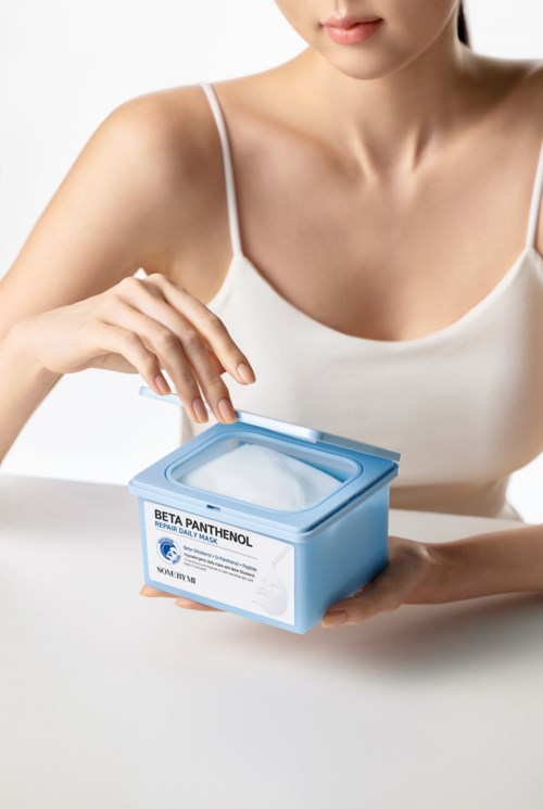 A woman in a white top holds a blue container labeled 'Beta Panthenol' on a white surface.