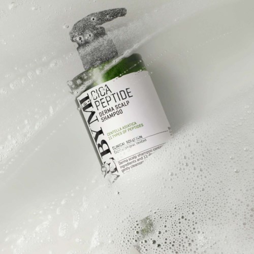 A green and white bottle of scalp shampoo with a pump, immersed in soapy water.