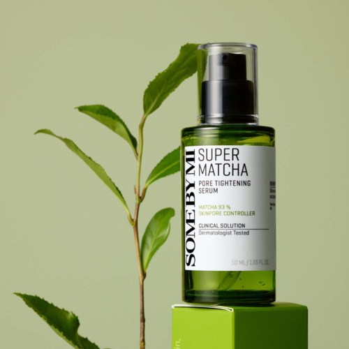 Groene glazen fles met pomp, labeled Super Matcha pore tightening serum, naast een groene doos en een theeplantblad.