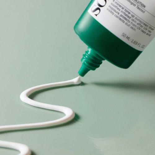 Een groene huidverzorgingstube die witte crème uitknijpt op een lichtgroene ondergrond.