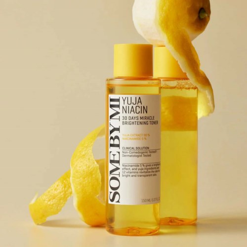 Two yellow bottles of skincare serum with lemon peel slices next to and on top. One bottle has a label.