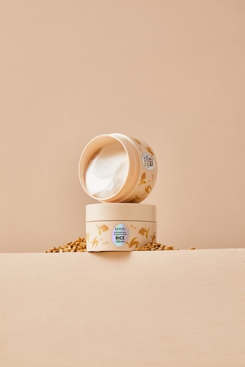 Eine Cremetiegel mit Kuhillustration, offenen Deckel und laufender Creme, auf einer cremefarbenen Oberfläche.