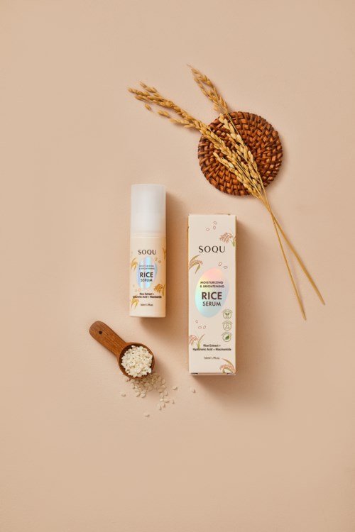 Produkt serum ryżowy z opakowaniem, butelką, łyżeczką i suszonymi źdźbłami pszenicy na beżowym tle.