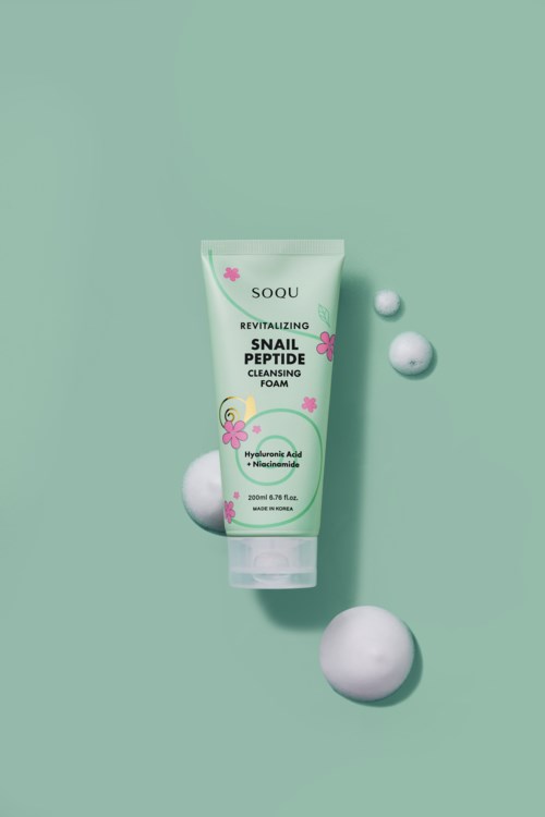 En tube med ansiktsrensskum med rosa blomster og grønne blader, merket 'Snail Peptide Cleansing Foam,' omgitt av hvite bobler.