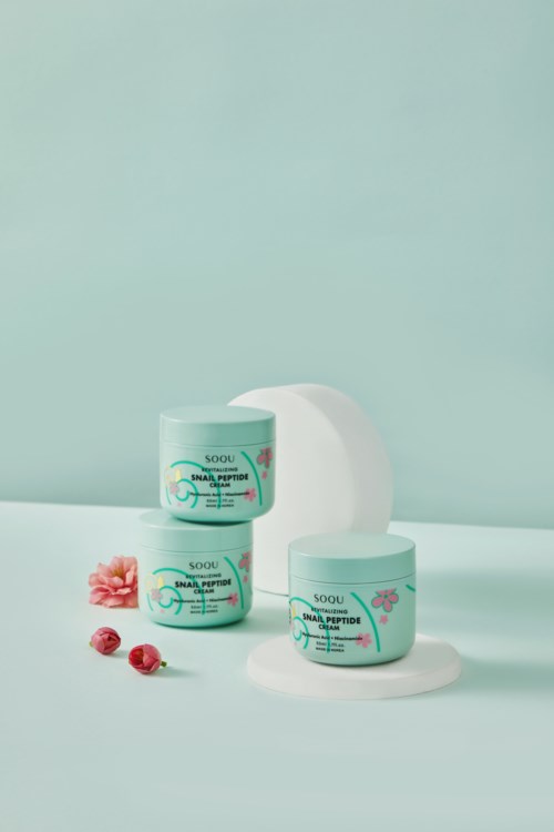 Two skincare jars with pink and blue labels, placed on a light blue background, with some pink flowers and berries.