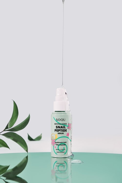 A dropper bottle of snail peptide serum with green leaves nearby, placed on a two-tone background.
