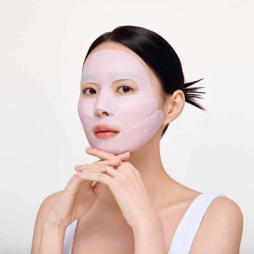 Eine Frau trägt eine weiße Gesichtsmaske auf, konzentriert auf ihr Gesicht, mit dunklen Haaren und neutralem Hintergrund.