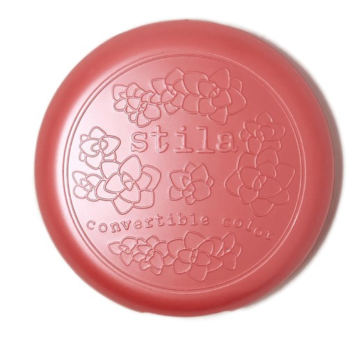 A pink, round product with flowers, the word 'stila,' and 'convertible color' embossed on it.