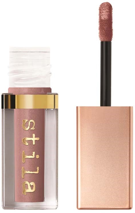 Een lippenstift met doorzichtige verpakking en nude tint, met applicator ernaast. Merkenaam staat op de verpakking.