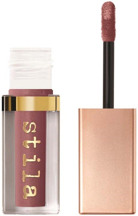 Een lipgloss met een roze tint. De tube heeft een gouden band en de merknaam erop. De applicator staat ernaast.