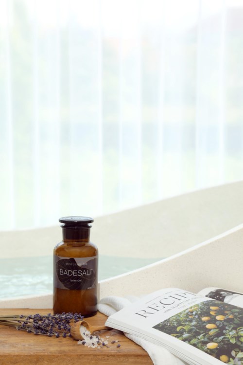 A small brown bottle labeled 'Radesalt' next to a book and lavender flowers on a wooden surface.